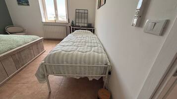 Ein Schlafzimmer mit einem Einzelbett, einem Heizkörper, einem Fenster und einem kleinen Hocker.