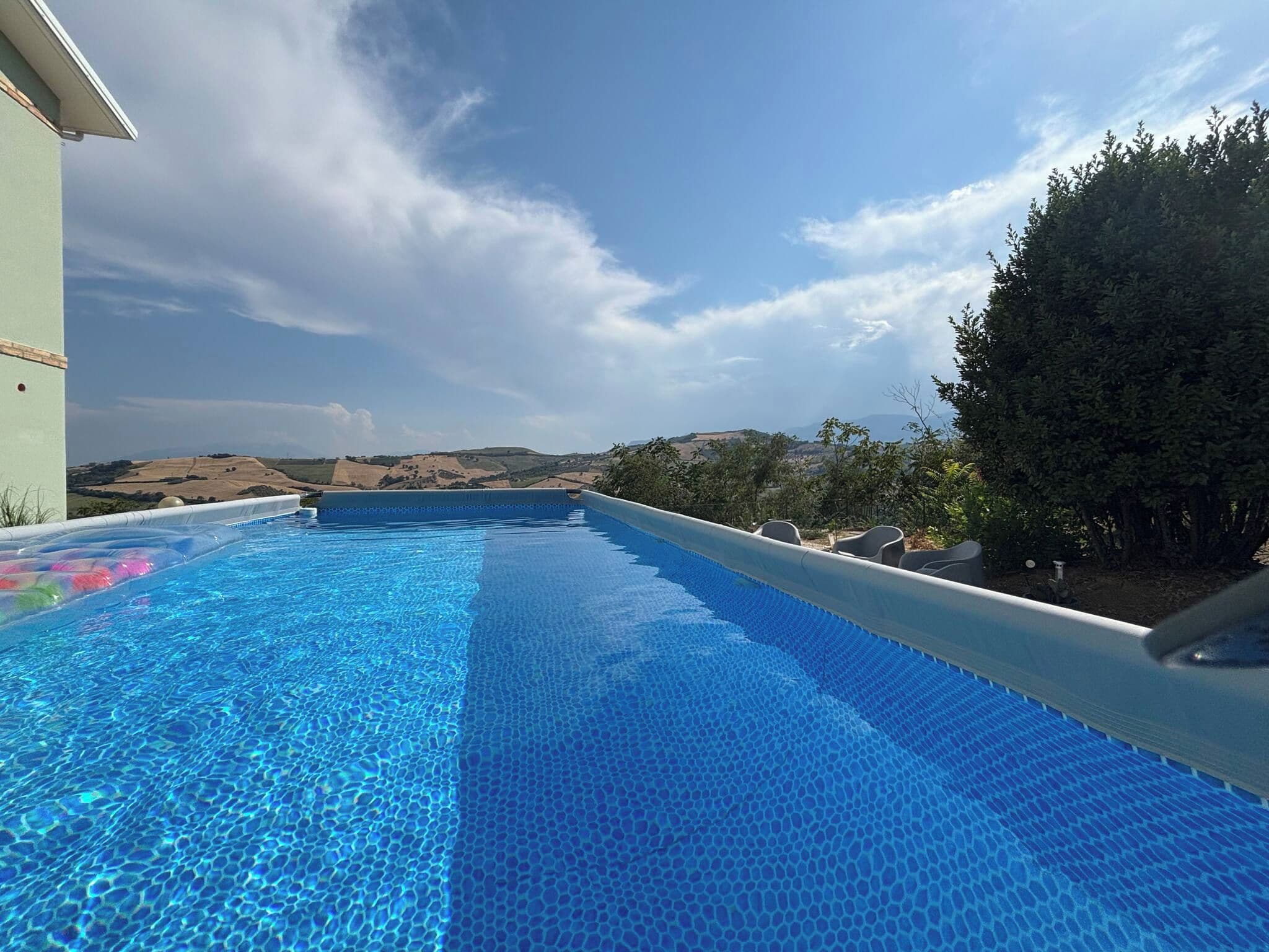 A swimming pool with a clear blue water surface, surrounded by a landscaped garden and a view of distant hills.