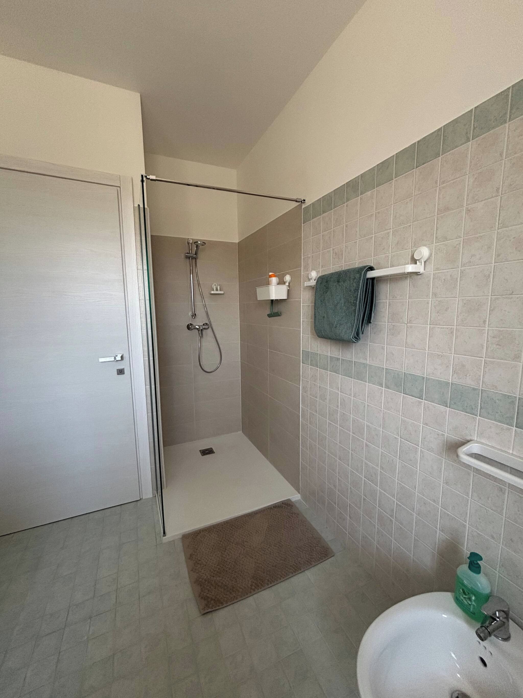 A bathroom with a shower, sink, and towel rack.