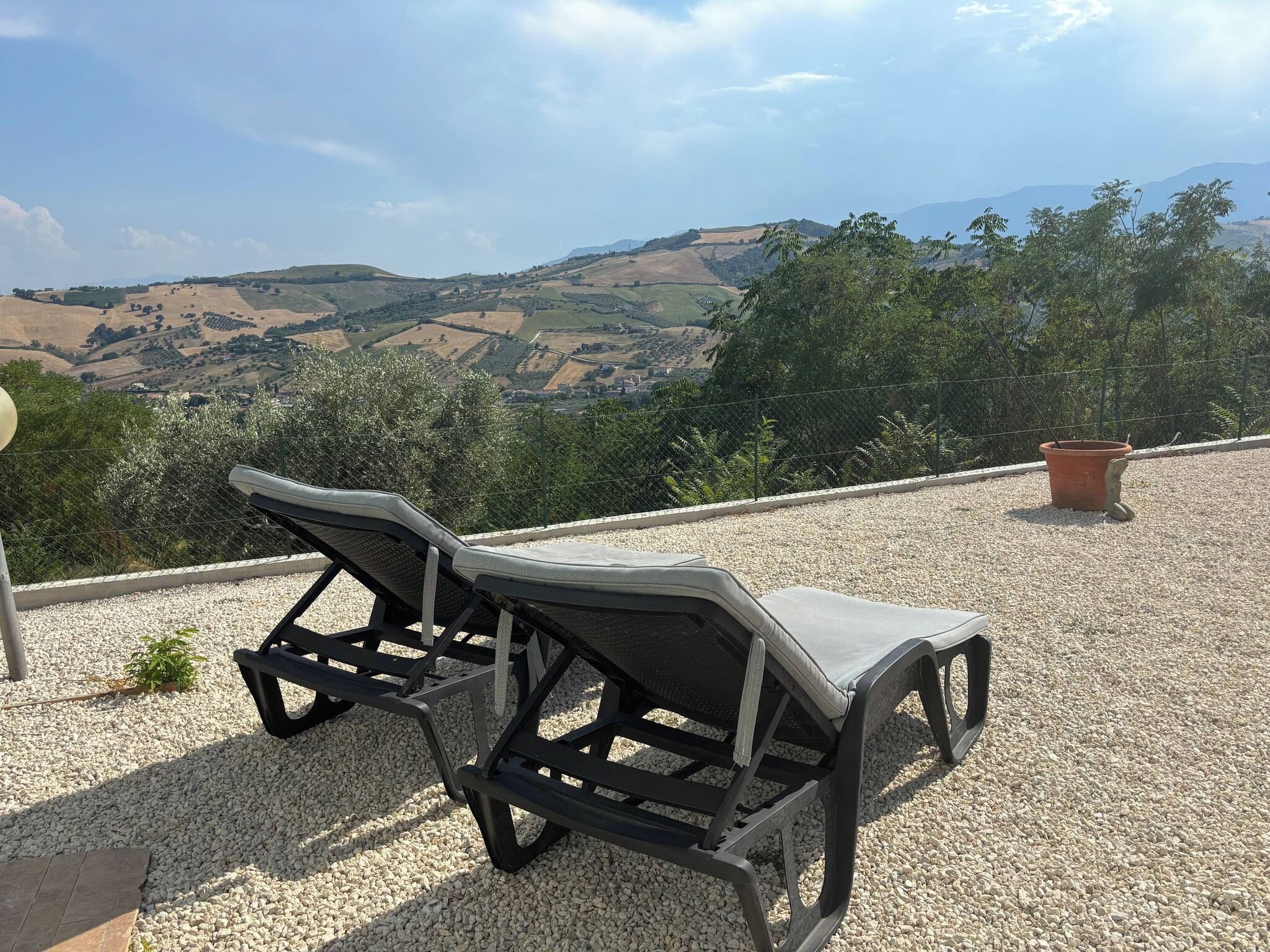 Two outdoor lounge chairs on a gravel surface with a view of rolling hills and a clear sky.