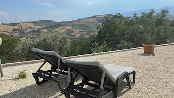 Two outdoor lounge chairs on a gravel surface with a view of rolling hills and a clear sky.