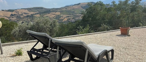 Two outdoor lounge chairs on a gravel surface with a view of rolling hills and a clear sky.