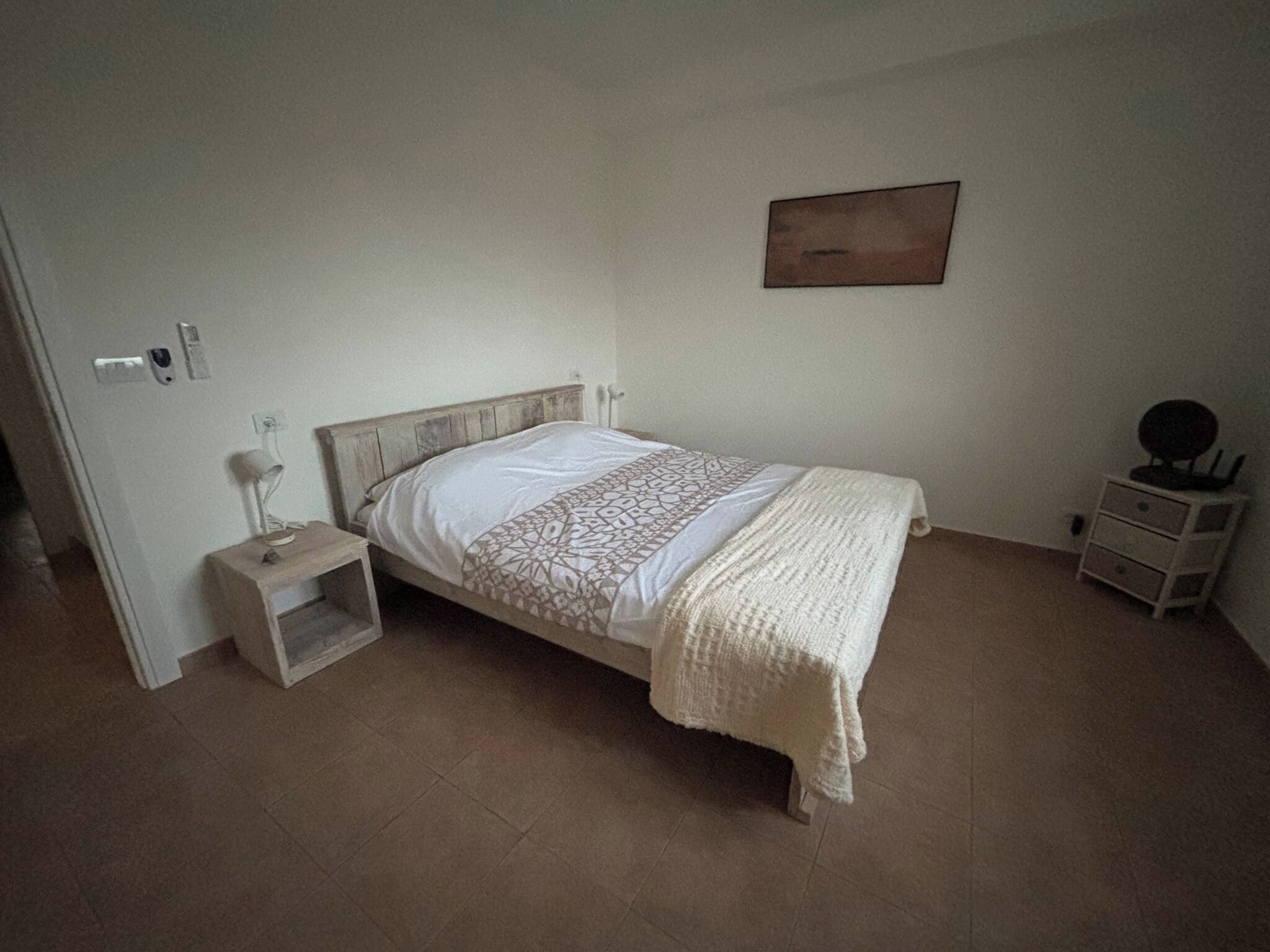 A bedroom with a bed, a bedside table, a nightstand, a wall-mounted lamp, and a small cabinet.