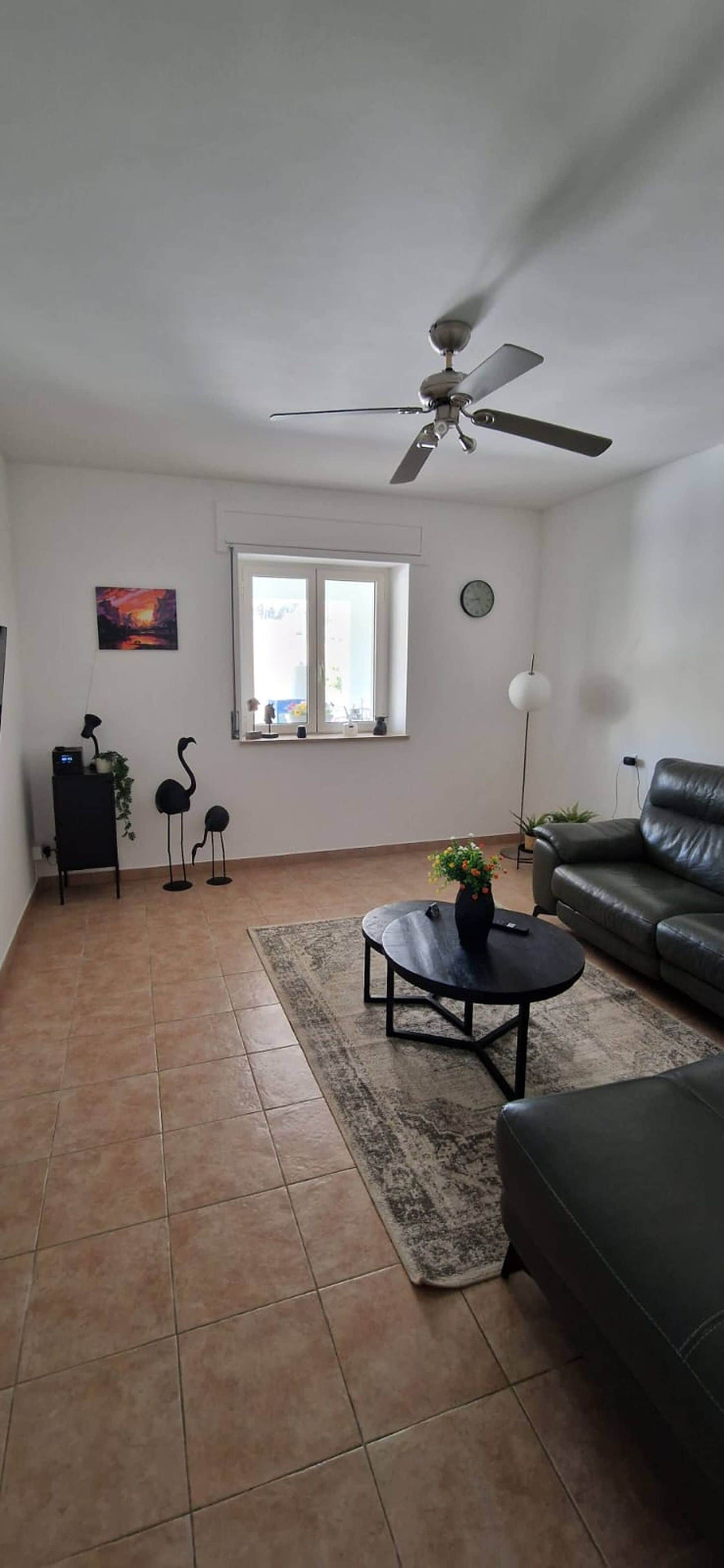 A living room with a ceiling fan, a sofa, a coffee table with a plant, and a window with a view.