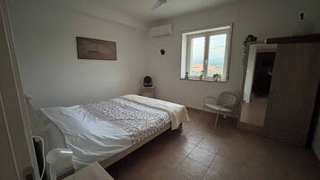 Quarto com cama, cadeira, escrivaninha, janela com vista e ventilador de teto.