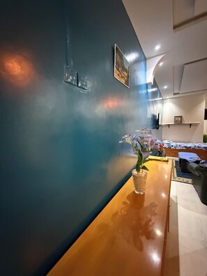 A room with a wooden table, a vase with flowers, a bed with a floral bedspread, and a wall with a painting. - Villa Soleil du Sénégal : Blue Loft (Dakar)