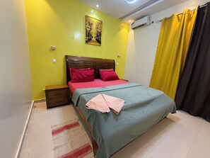 Ein Schlafzimmer mit einem Bett, einem Nachttisch, einer Wand-Klimaanlage und einem Gemälde.