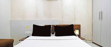 Habitación de hotel con cama, mesita de noche, lámpara, armario y unidad de aire acondicionado.