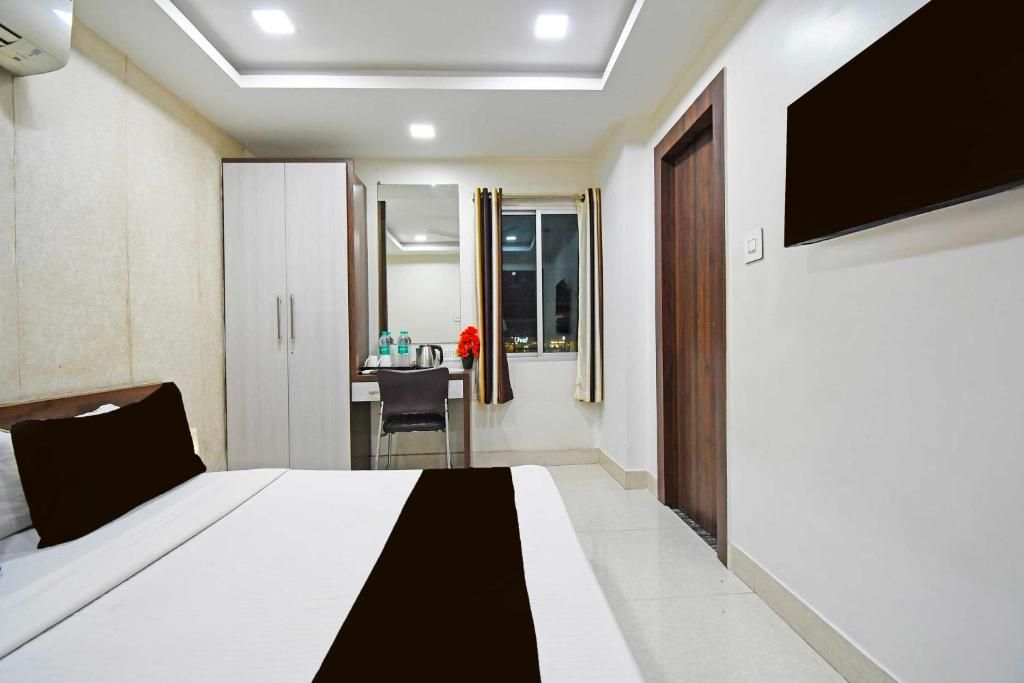 Quarto de hotel com cama, escrivaninha, cadeira, janela com cortinas e televisão na parede.