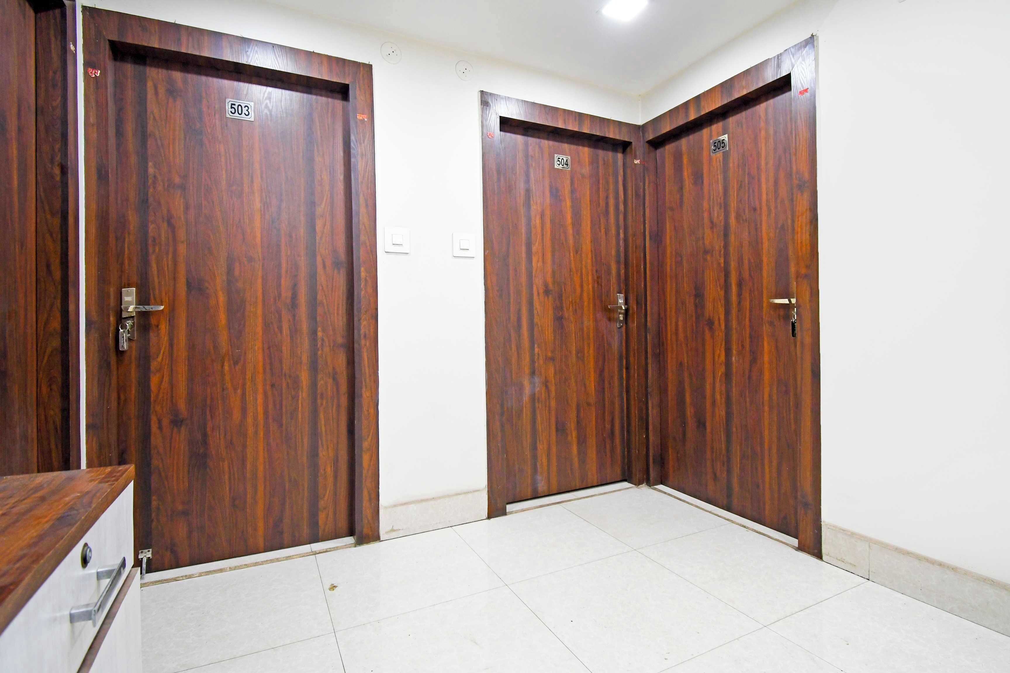 Un pasillo con dos puertas de madera, cada una con un número, y un piso cubierto de baldosas blancas.