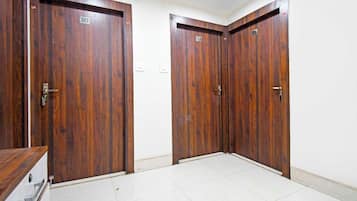 Un pasillo con dos puertas de madera, cada una con un número, y un piso cubierto de baldosas blancas.