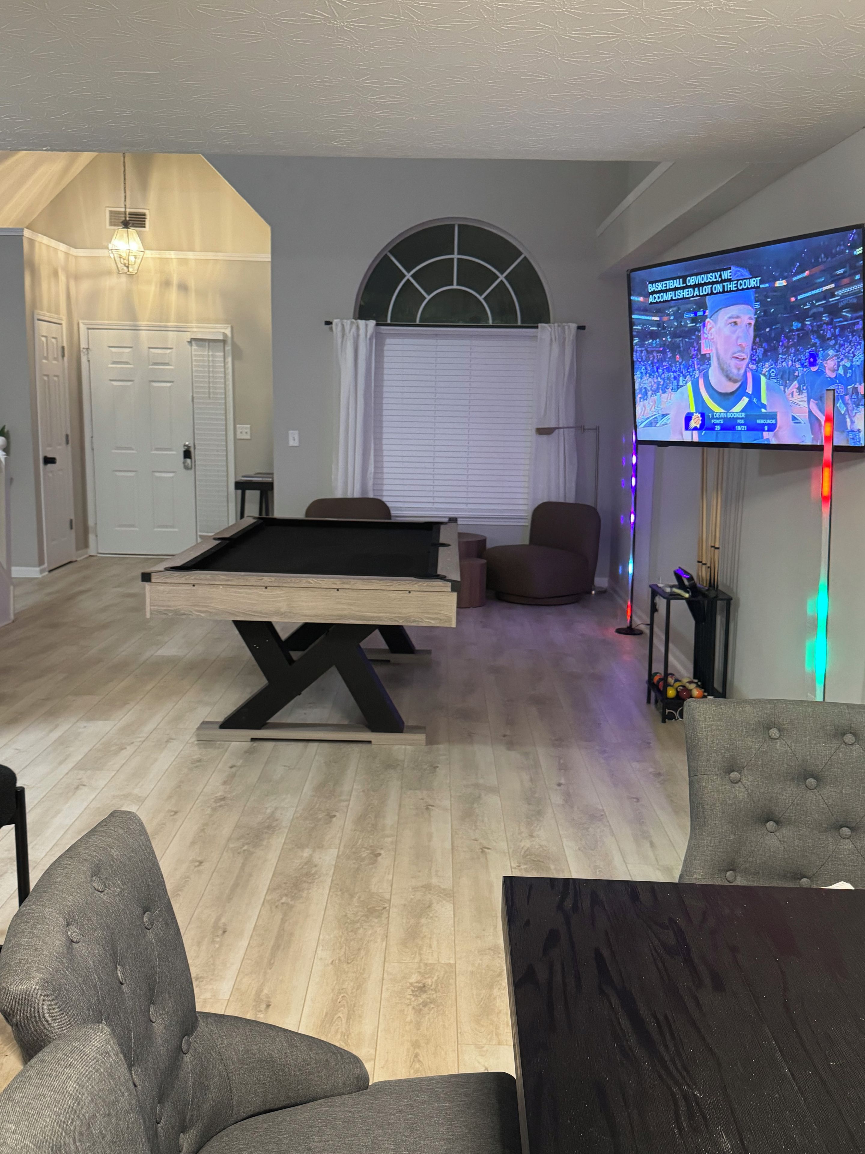 A living room with a pool table, a television displaying a sports game, and a seating area with chairs.