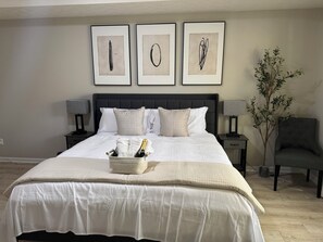 Ein ordentlich bezogenes Bett mit weißer Decke und Kissen, ein Nachttisch mit Lampe und eine Zimmerpflanze.