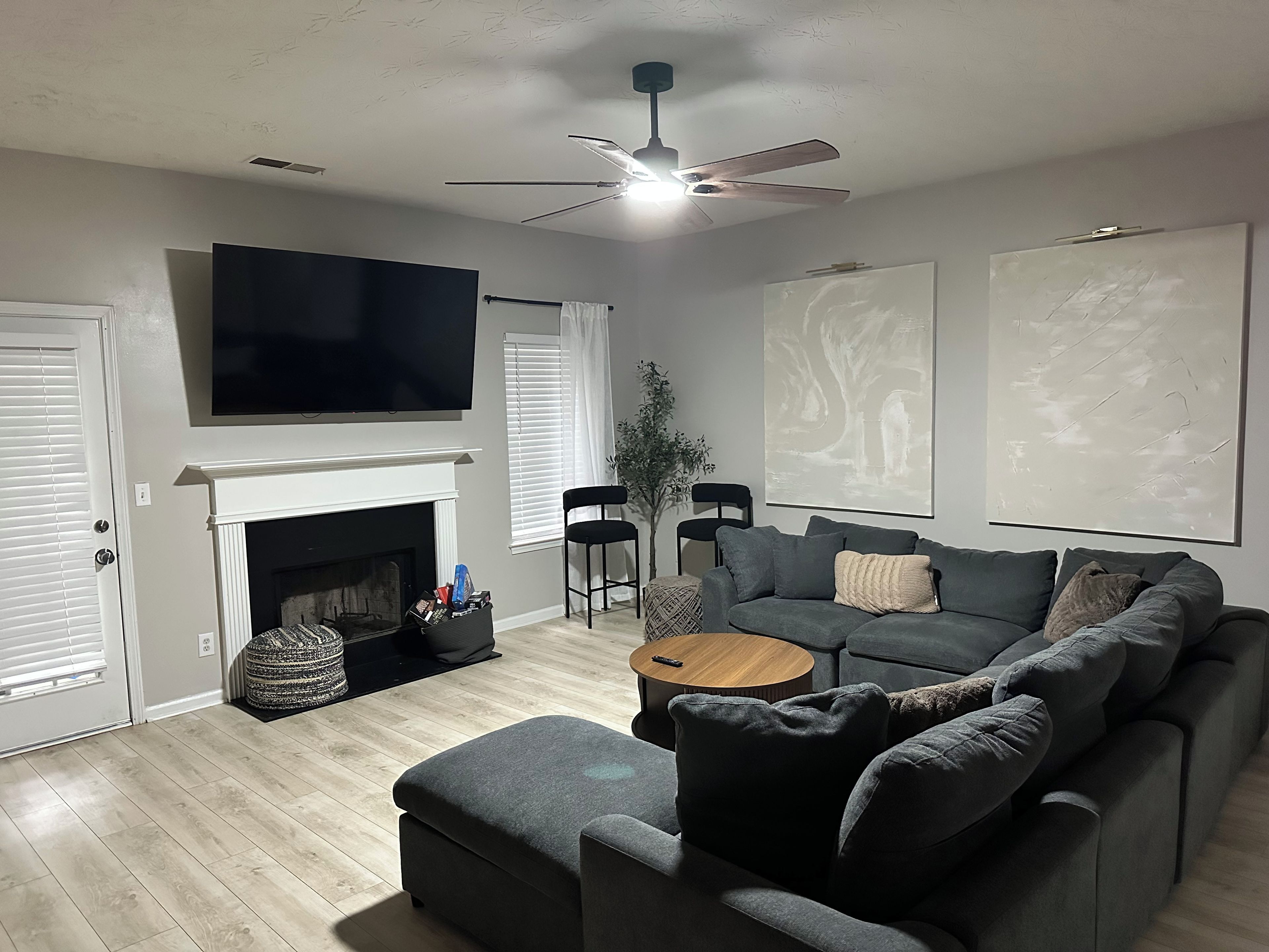 Un salon doté d’une cheminée, d’un téléviseur à écran plat, d’un ventilateur de plafond et d’un grand tableau accroché au mur.