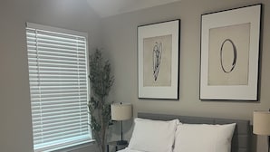 Ein Schlafzimmer mit einem Bett, einem Deckenventilator, einem Fenster mit Jalousien und zwei gerahmten Kunstwerken an der Wand.