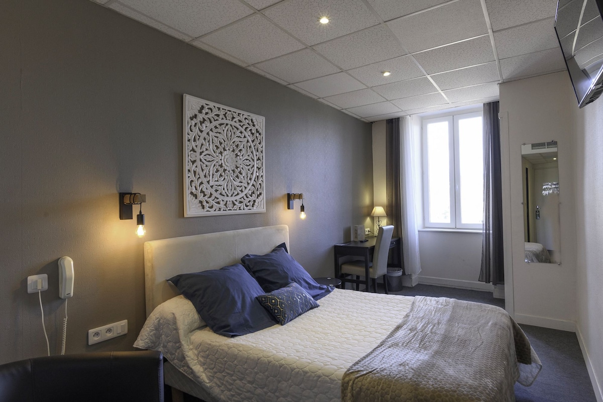 Quarto de hotel com cama, abajures, escrivaninha e janela.