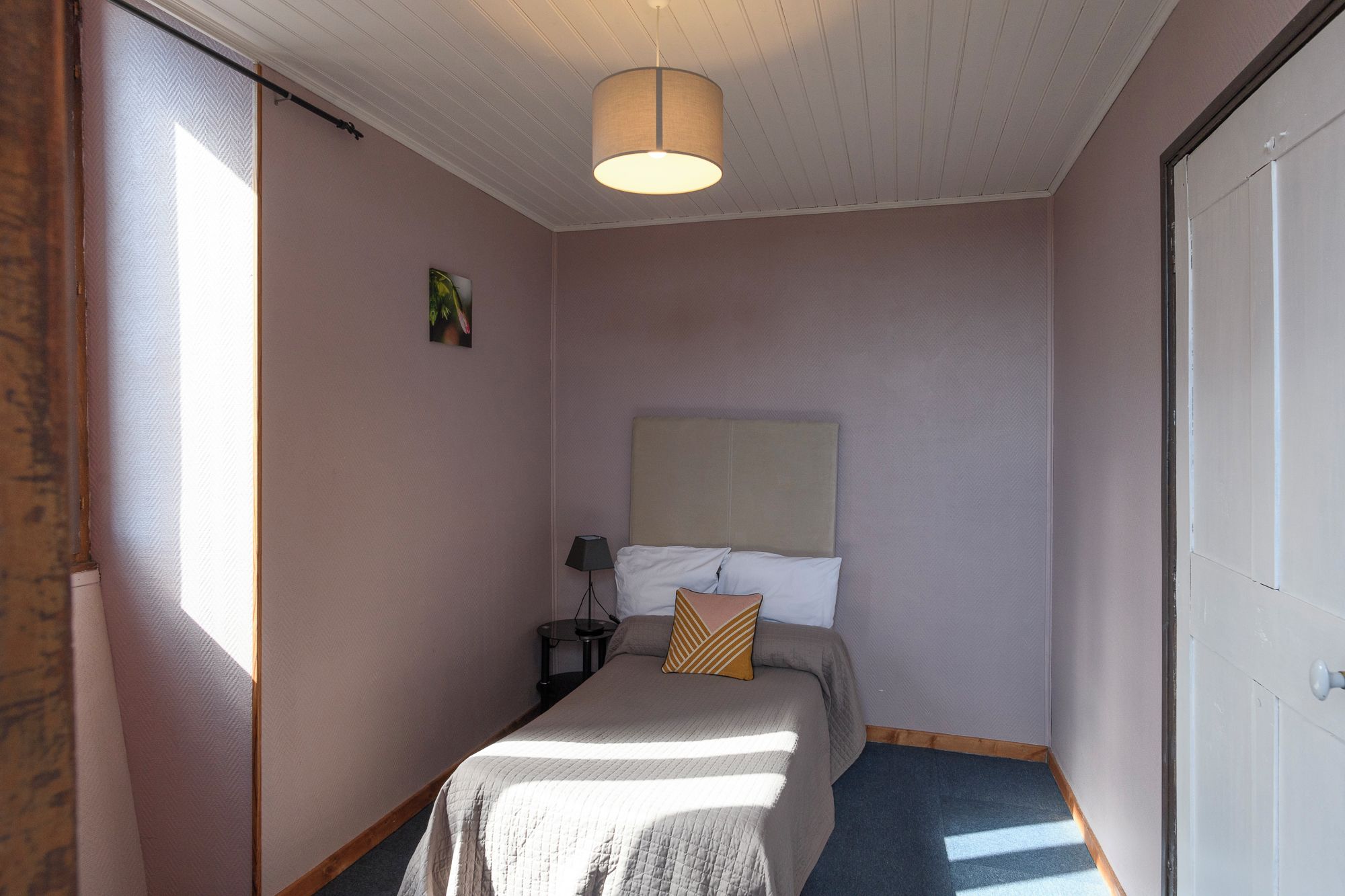A bedroom with a bed, a nightstand, a lamp, and a door.