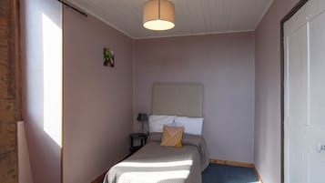 A bedroom with a bed, a nightstand, a lamp, and a door.