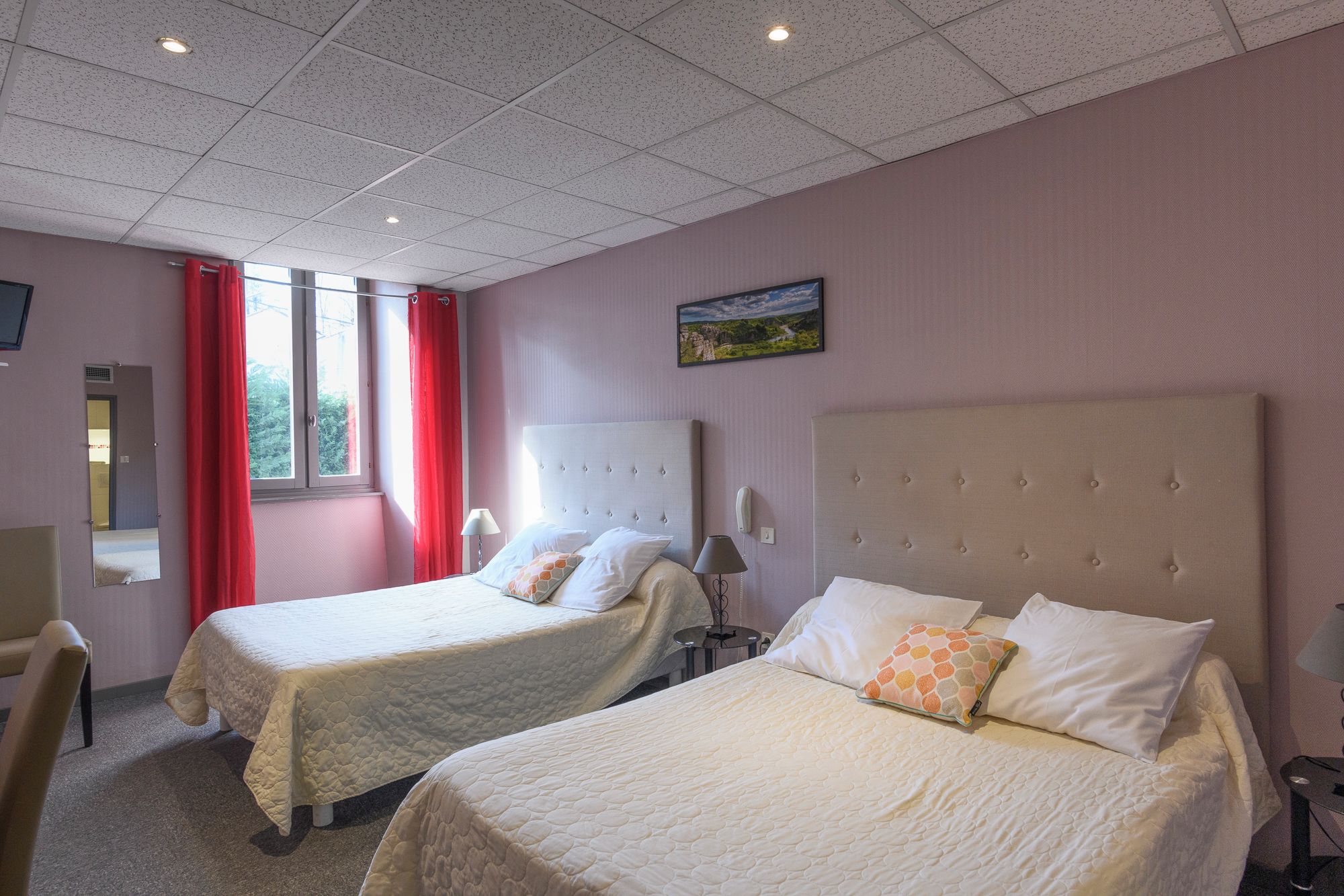 A hotel room with two beds, a window with red curtains, a bedside lamp, and a painting on the wall.