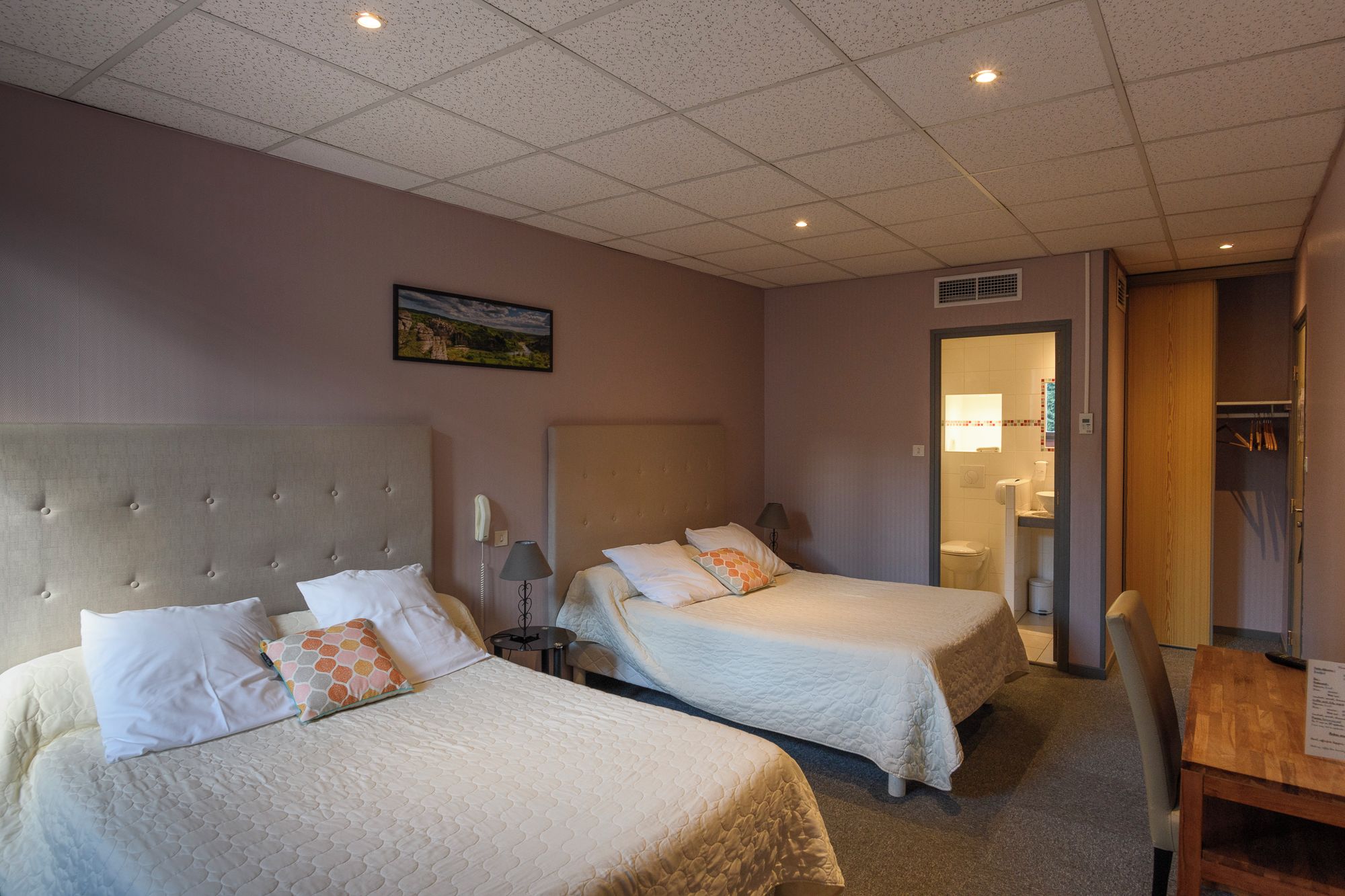 Une chambre d’hôtel avec deux lits, un bureau et une salle de bain visible à travers une porte ouverte.