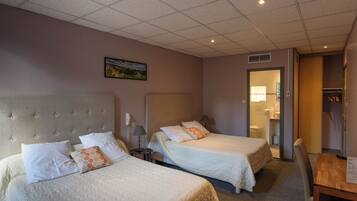 Une chambre d’hôtel avec deux lits, un bureau et une salle de bain visible à travers une porte ouverte.