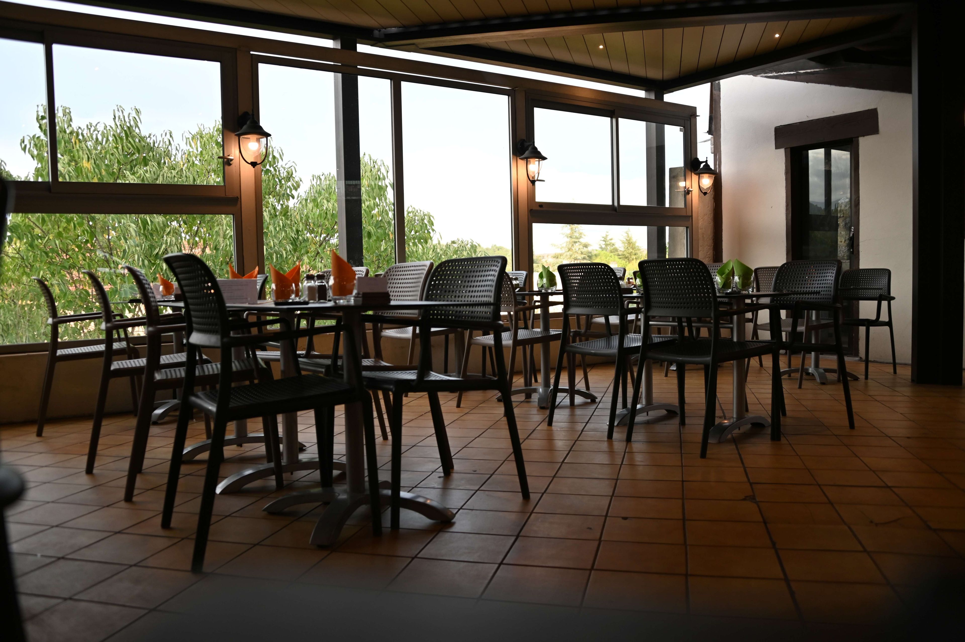Restaurante com área externa, grandes janelas e piso ladrilhado.