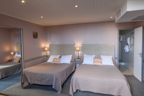 Quarto de hotel com duas camas, luminárias de cabeceira, área de chuveiro e espelho.