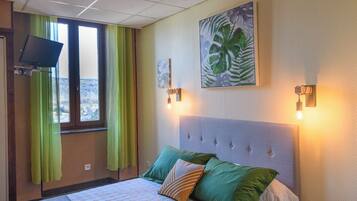 Een hotelkamer met een bed, groene gordijnen, een televisie en een schilderij aan de muur.