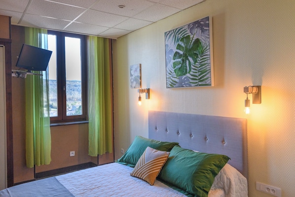 Habitación de hotel con una cama, cortinas verdes, un televisor y un cuadro en la pared.