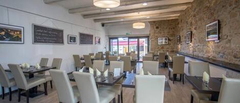 Un restaurante con varias mesas y sillas, una pared de piedra y cuadros en las paredes.