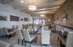 Um restaurante com várias mesas e cadeiras, uma parede de pedra e quadros nas paredes.