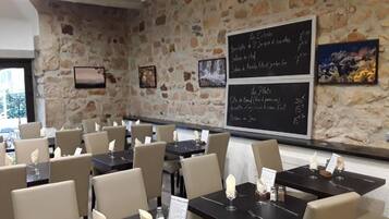 Een restaurantinterieur met stenen muren, gedekte tafels met witte servetten en zwarte menukaarten.