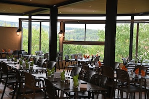 Un restaurante con terraza, mesas con sillas y vistas a zonas verdes.