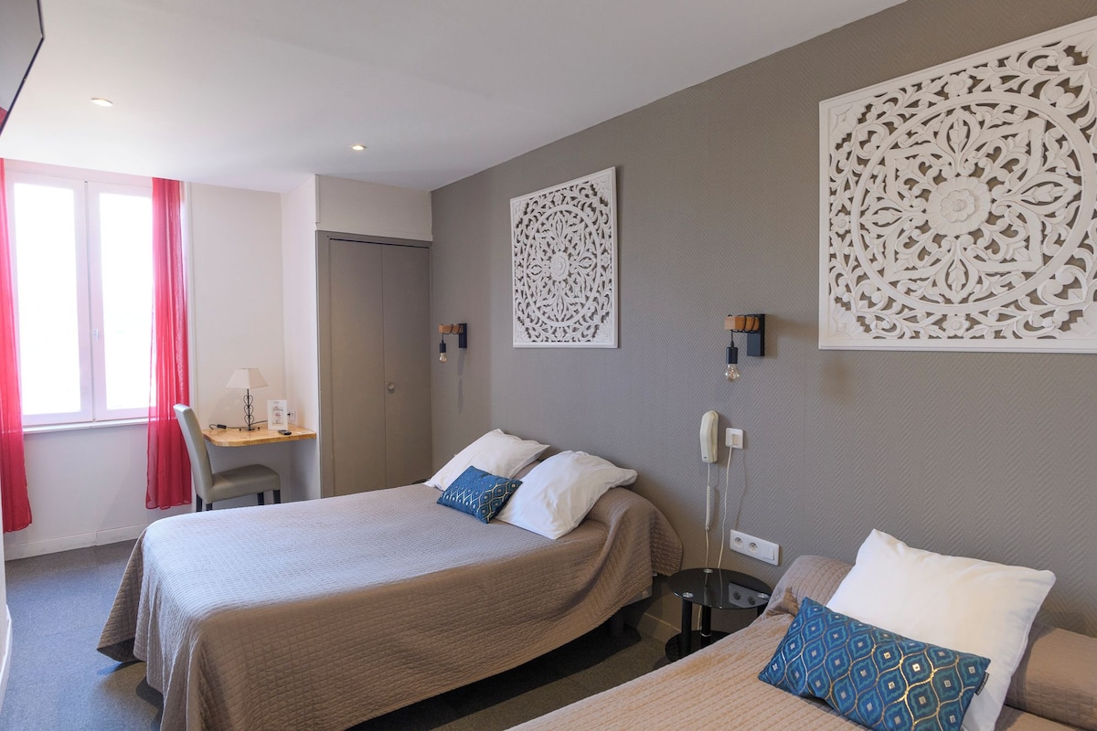 Quarto de hotel com cama, mesas de cabeceira, escrivaninha e painéis decorativos na parede.