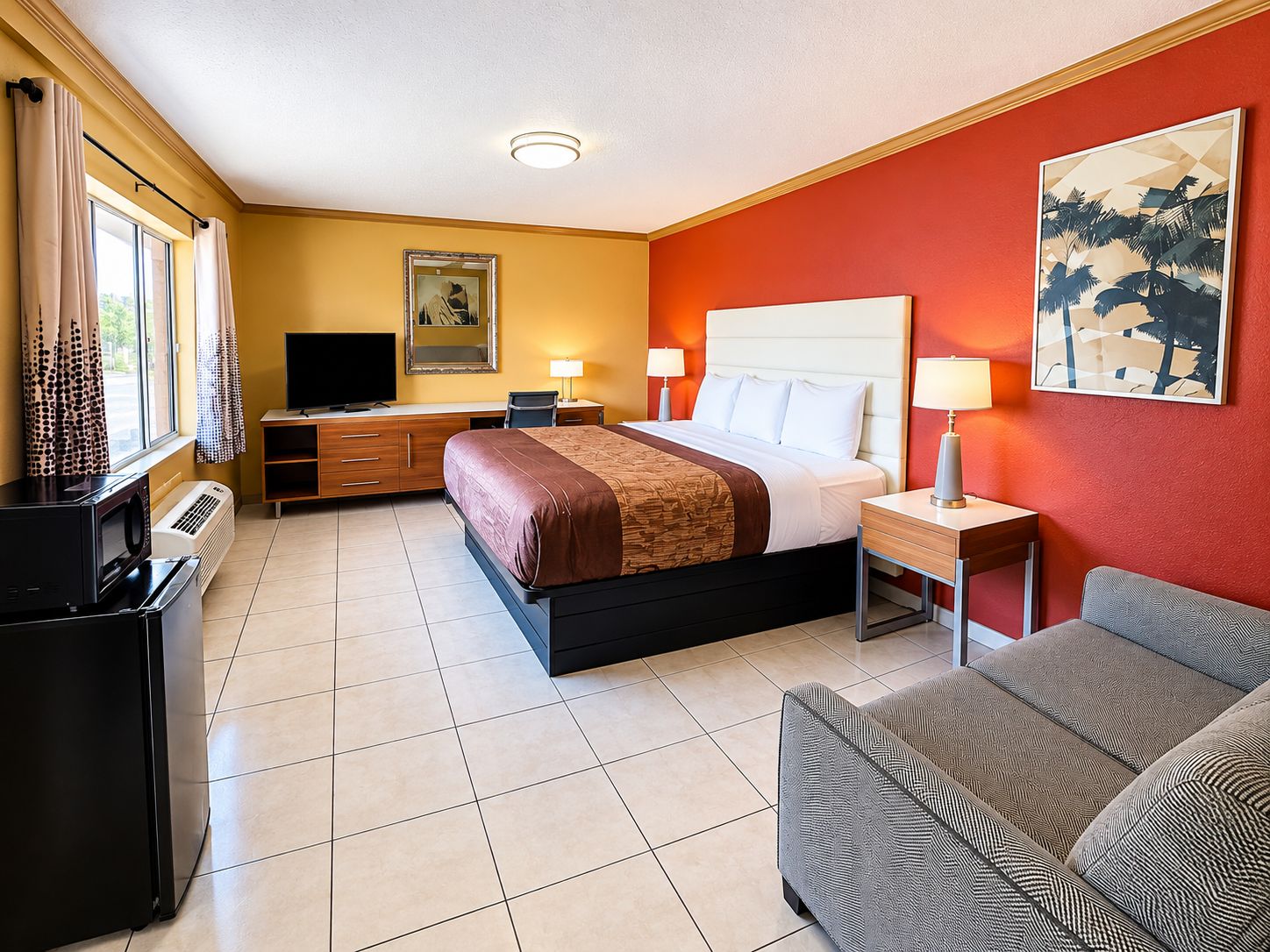 Quarto de hotel com cama, mesas de cabeceira, televisão, escrivaninha e sofá.