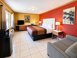 Una habitación de hotel con una cama, mesitas de noche, un televisor, un escritorio y un sofá.