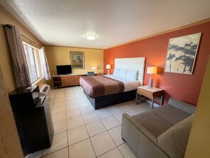 A hotel room with a bed, a desk, a chair, a TV, and a painting on the wall. - North Port INN (North Port)