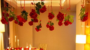 A hotel room with a dining table set for two, a bed with rose decorations and balloons, and a wall adorned with hanging roses. - Résidence Jasmins  (Oran)