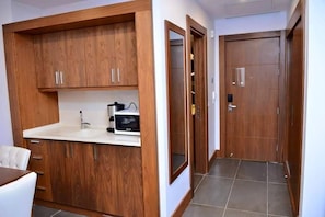 A wooden kitchen with a white countertop and cabinets, a black appliance, and a door with a handle.