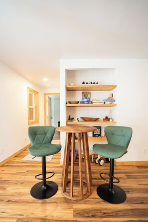 Een eethoek met twee groene stoelen, een houten tafel en planken met boeken en decoratieve objecten.