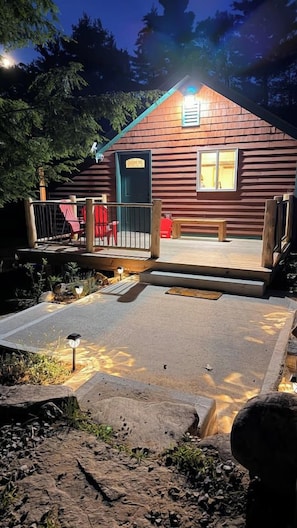 A cabin with a wooden deck, a bench, and a small outdoor area with a paved path. - Last-Minute Fall Escape · Game Room & Fire Pit (Jay)