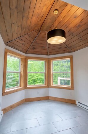 A room with a sloped ceiling, three large windows, and a central light fixture. - Whiteface Getaway | Fire Pit, Game Room, Bunk Room (Jay)