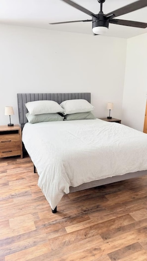 A bedroom with a bed, wooden flooring, a ceiling fan, and bedside lamps. - Last-Minute Fall Escape · Game Room & Fire Pit (Jay)