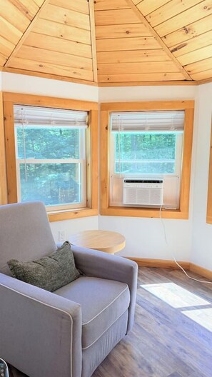 A room with a grey sofa, a small round table, and two windows with blinds. - Whiteface Getaway | Fire Pit, Game Room, Bunk Room (Jay)