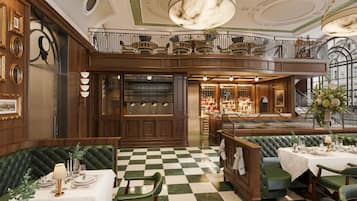 Un'imponente hall d'albergo con pavimento a scacchi, un'area bar e un balcone con ringhiere decorate.