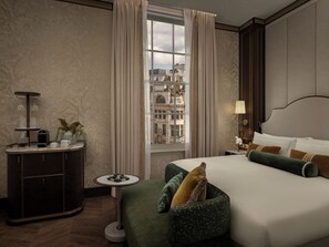 A hotel room with a large bed, a desk with a lamp, a small table, and a view of a cityscape through a window. - The WestDill Mayfair Hotel London, Colbert Collection (London)