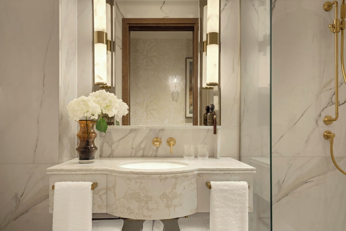 A bathroom with a marble vanity, a large mirror, a gold shower, and white towels.