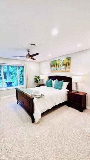 A bedroom with a bed, a nightstand, a ceiling fan, a window with a view, and a painting on the wall. - Cozy Retreat On The Eastside Estate (sleeps 4) (Greater Napanee)