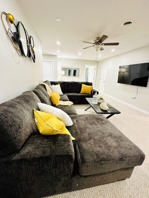 A living room with a sectional sofa, a coffee table, and a flat-screen TV mounted on the wall. - Cozy Retreat On The Eastside Estate (sleeps 4) (Greater Napanee)