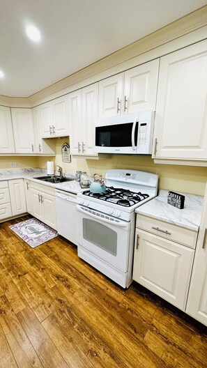 Una cocina con armarios blancos, una estufa blanca, un microondas y piso de madera.